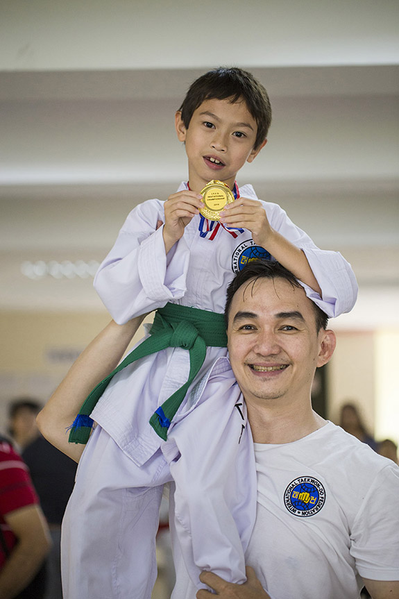 Anak kecil pemenang mendali emas beladiri TaekwonDo ITF memamerkan mendali bersama pelatih.